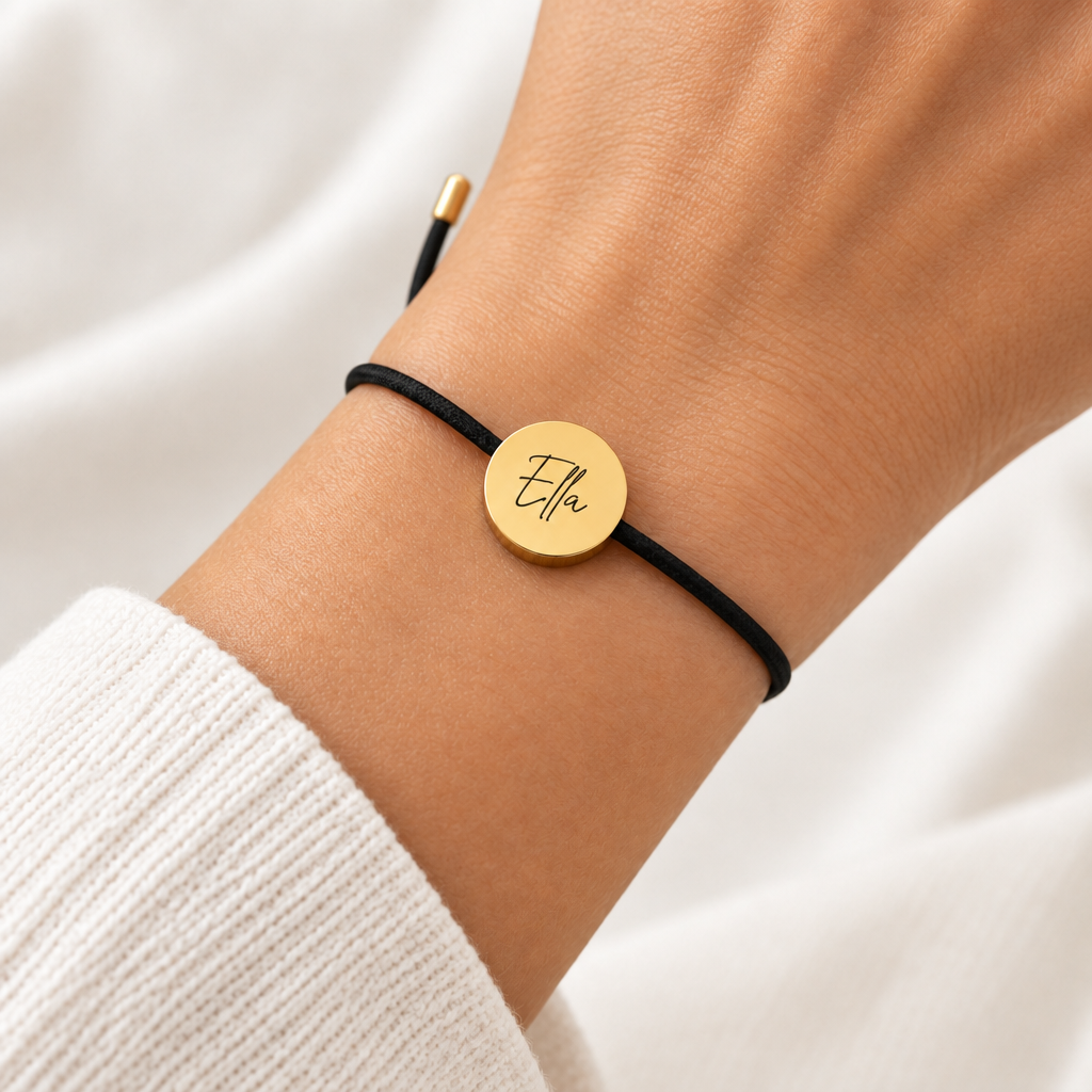 A black adjustable cord bracelet with a round gold-tone disc charm engraved with the name 'Ella', displayed on a clean white background.